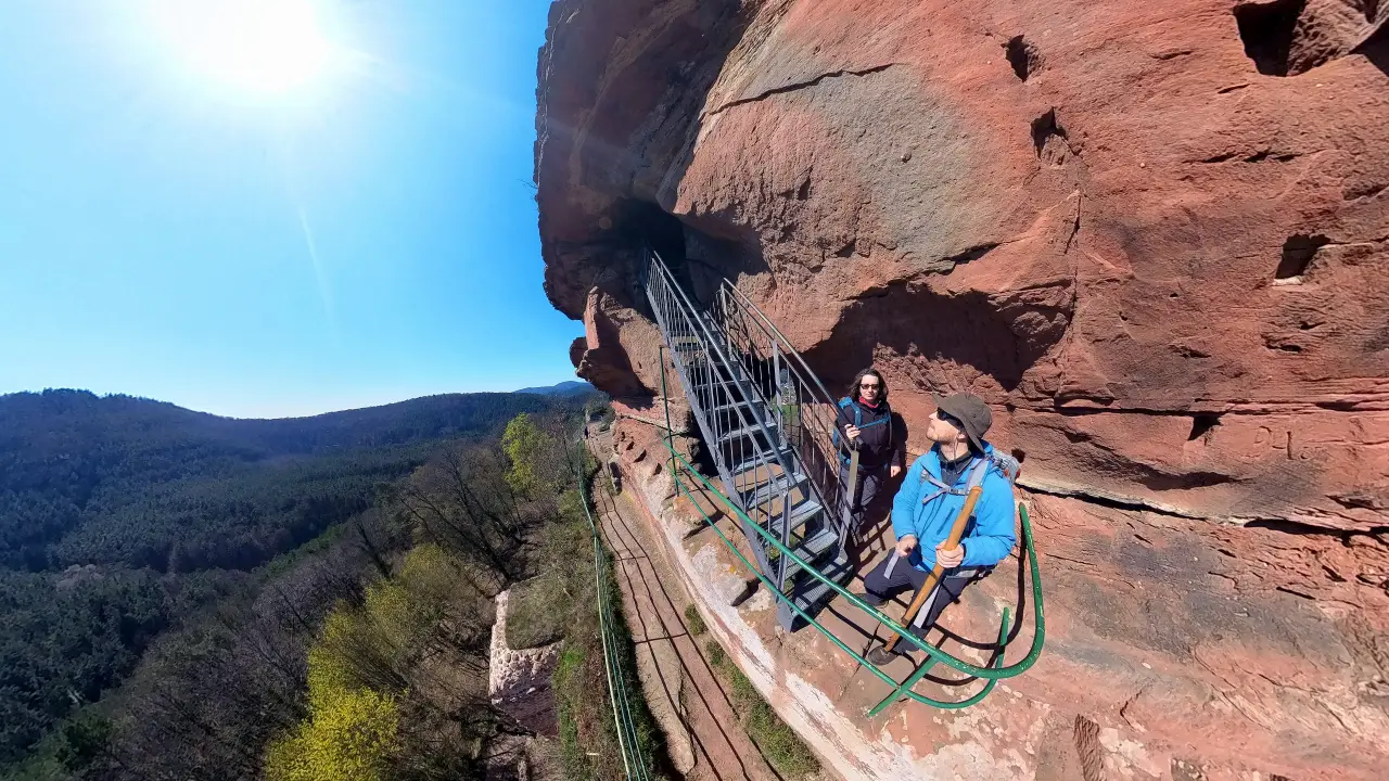 Selfie of Manu and Markus on the side of the rock needle high above the valley. Behind us a stair is leading into the rock.