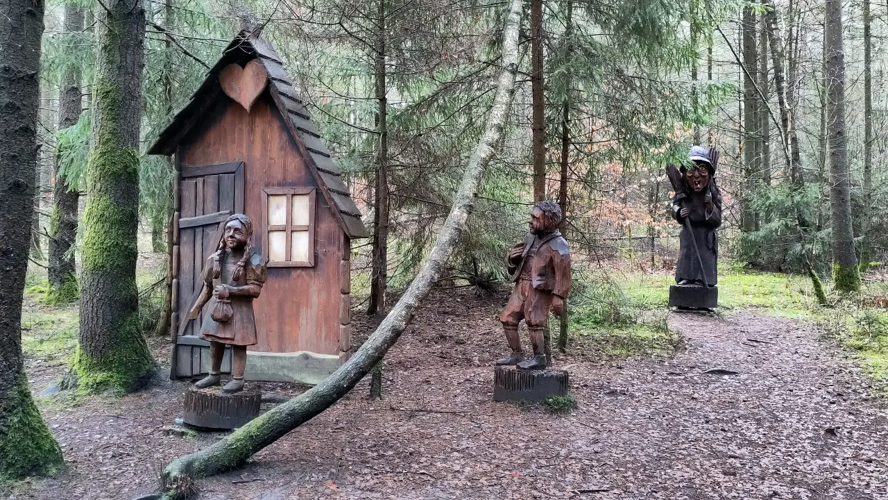 A group of sculptures with Hansel and Gretel in front of the witch's hut. The with looks on from the background.