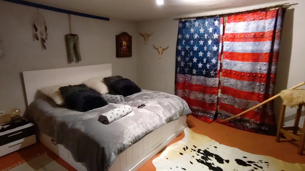 A room at the Longhorn Ranch. A large bed, the walls and curtains in stereotypical american style with flags, animal skulls etc.