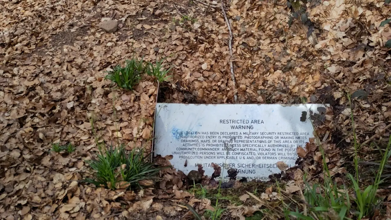 A half-buried sign with a bilingual text (English and German) designating a military restriction zone