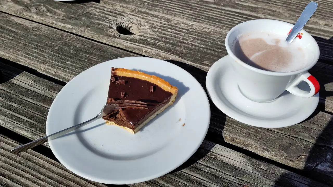 A cup of hot chocolate and a half-eaten piece of chocolate tarte on a wooden table