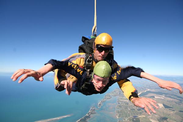 Markus unter seinem Tandemmaster im freien Fall. Im Hintergrund ist die Küste und das blaue Meer zu erkennen