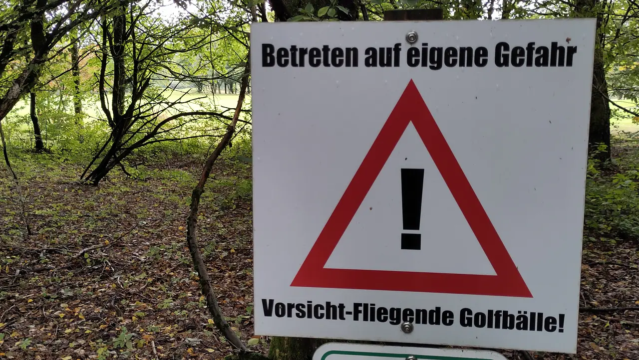 Ein Schild mit der Aufschrift "Betreten auf eigene Gefahr. Vorsicht-Fliegende Golfbälle!