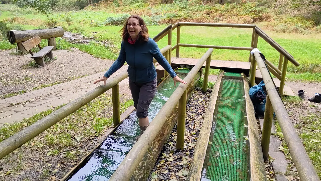 Manu im Kneippbecken. Sie lacht leicht schmerzverzerrt. Offenbar ist das Wasser ordentlich kalt.