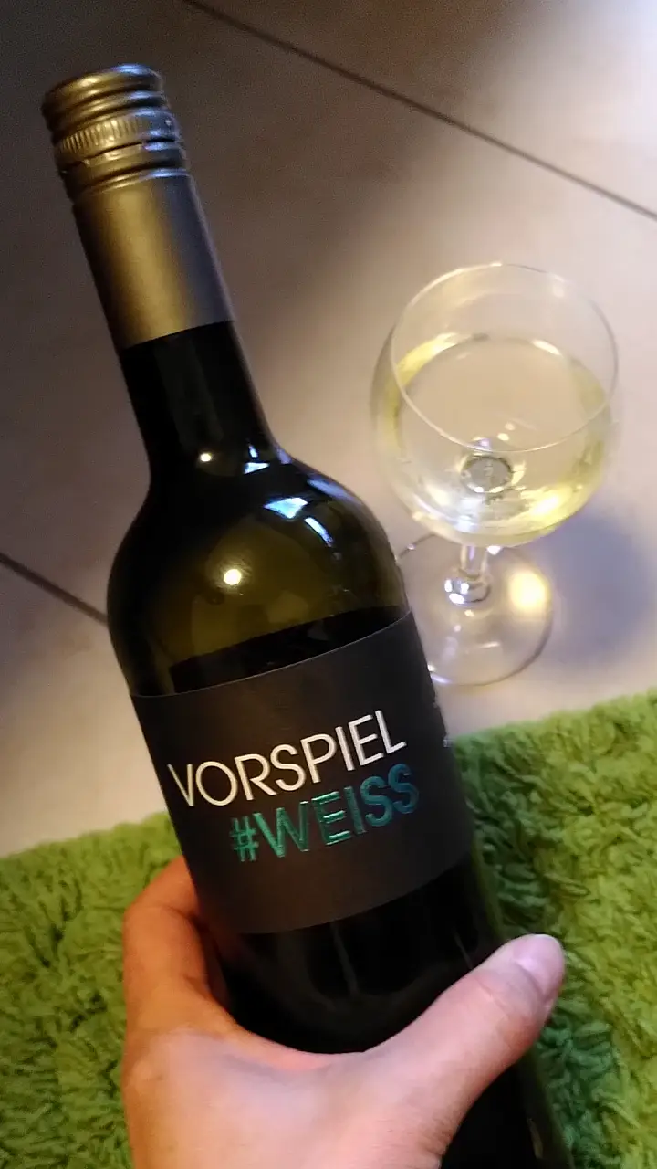 Manu hält eine Flasche mit der Aufschrift "Vorspiel #Weiss" in der Hand